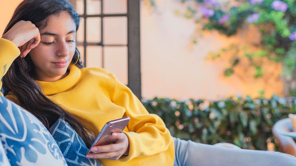 Teenage girl sitting outdoors looking at her phone for online therapy